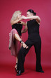 Beautiful blond and brunet dancing salsa on red background