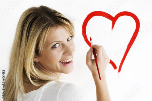 wsmiling young woman drawing heart-shape on white wall wsmiling young woman drawing heart-shape on white wall