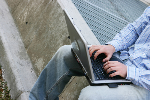 Photo: young man sitting while typing on laptop young man sitting while typing on laptop