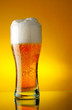 Glass of beer close-up with froth over yellow background