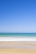 Sandy beach and surf of green sea with bright blue sky