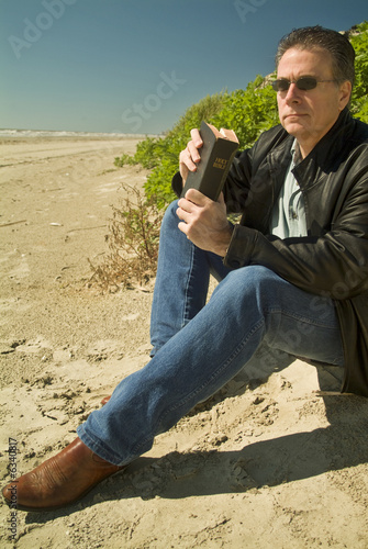 Photo: A man holding a bible, sitting at the edge of a sand dune. A man holding a bible, sitting at the edge of a sand dune.