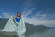 Woman extending a tablecloth for a picnic at the edge of a lake