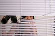 Woman peering through blinds with binoculars