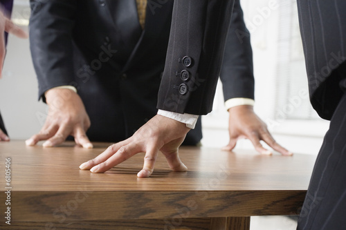 Photo: Midsection of people standing around a table. Midsection of people standing around a table.