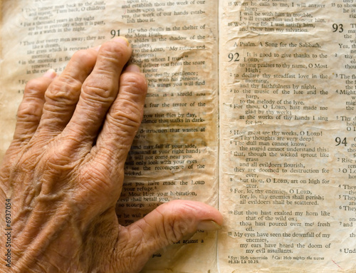 Photo: Wrinkled arthritic hand on opened old bible Wrinkled arthritic hand on opened old bible