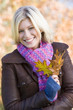 Woman outdoors at park holding leaves in hand smiling
