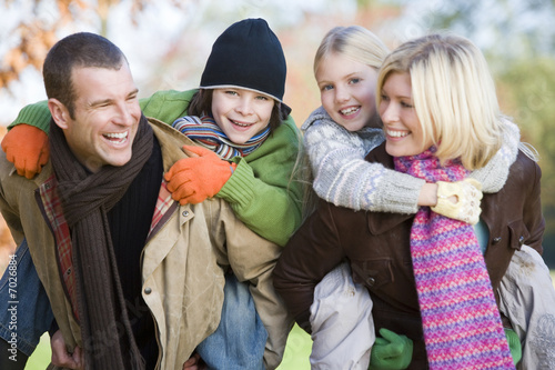 Foto: Parents outdoors piggybacking two young children and smiling Parents outdoors piggybacking two young children and smiling