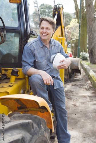 Photo: A happy smiling builder sitting on his digger. A happy smiling builder sitting on his digger.
