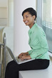 Business woman using laptop sitting on window ledge, side view