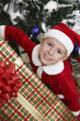 Boy 5-6 in Santa costume holding present by Christmas tree