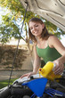 Young woman pouring oil into car engine