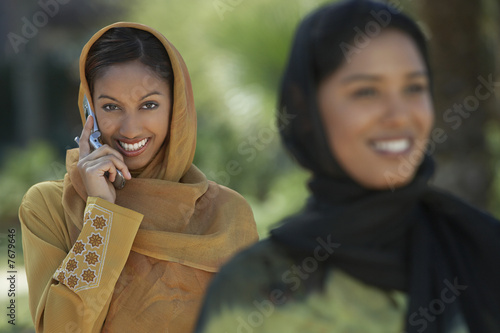 Photo: Two muslim woman, smiling, one talking on mobile, selective focus Two muslim woman, smiling, one talking on mobile, selective focus
