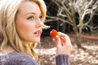 Beautiful young woman eating a strawberry in the park