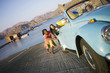 Photo: Two teenage girls (17-19) pushing blue car, lake in background, teenage boy steering (tilt) Two teenage girls (17-19) pushing blue car, lake in background, teenage boy steering (tilt)