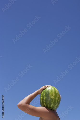 Photo: Man carrying watermelon on shoulder, face obscured, profile, clear blue sky in background Man carrying watermelon on shoulder, face obscured, profile, clear blue sky in background