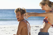 Photo: Teenage couple (17-19) sunbathing on beach, girl squirting suncream on boy's back, laughing Teenage couple (17-19) sunbathing on beach, girl squirting suncream on boy's back, laughing