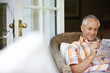 Photo: Mature man relaxing in wicker chair at home, doing newspaper crossword, smiling, focus on background Mature man relaxing in wicker chair at home, doing newspaper crossword, smiling, focus on background