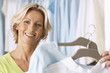 Photo: Mature woman shopping in clothes shop, holding two tops on coathangers, smiling, close-up, portrait Mature woman shopping in clothes shop, holding two tops on coathangers, smiling, close-up, portrait