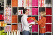 Photo: Couple shopping in department store, woman stacking multi-coloured towels in boyfriend's arms, smiling, side view, shelves in background Couple shopping in department store, woman stacking multi-coloured towels in boyfriend's arms, smiling, side view, shelves in background
