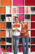 Photo: Couple shopping in department store, woman leaning against boyfriend, man holding pile of folded towels, smiling, front view, portrait, shelves in background Couple shopping in department store, woman leaning against boyfriend, man holding pile of folded towels, smiling, front view, portrait, shelves in background