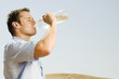 A man in a desert drinking from a bottle of water