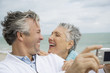 Foto: A senior couple on a beach taking a picture with a digital camera A senior couple on a beach taking a picture with a digital camera