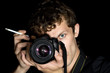 The young man - photographer behind work. Isolated on a black ba The young man - photographer behind work. Isolated on a black ba