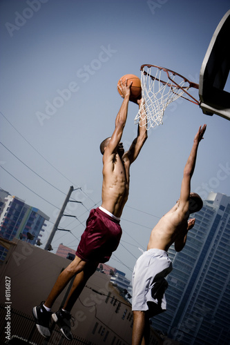Photo: Two Young African American man jumping with a basketball on an urban basketball court Two Young African American man jumping with a basketball on an urban basketball court