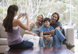 Foto: A young girl taking a photo of her family sitting on a sofa A young girl taking a photo of her family sitting on a sofa