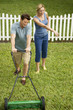man mowing the lawn, wife pointing at grass