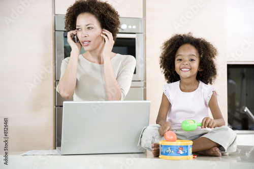 Photo: Stressed mother working from home while daughter plays a toy drum Stressed mother working from home while daughter plays a toy drum