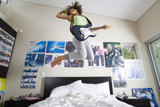 Photo: Teenage girl (16-18) playing electric guitar, jumping in air above bed, low angle view Teenage girl (16-18) playing electric guitar, jumping in air above bed, low angle view