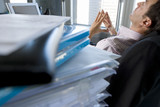 Photo: Young businessman leaning back in chair with hands together by files on desk (differential focus) Young businessman leaning back in chair with hands together by files on desk (differential focus)