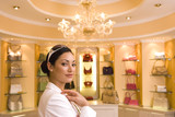 Photo: Young woman standing in front of designer handbags on shelf display in glamorous boutique, smiling, side view, portrait Young woman standing in front of designer handbags on shelf display in glamorous boutique, smiling, side view, portrait