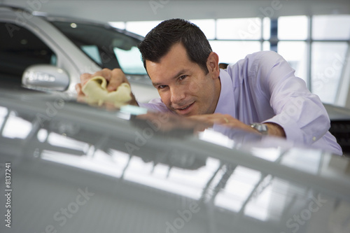 Photo: Car salesman polishing bonnet of new silver car with cloth in showroom (surface level) Car salesman polishing bonnet of new silver car with cloth in showroom (surface level)