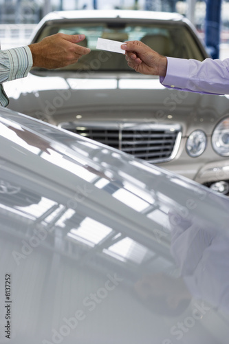 Photo: Car salesman passing business card to male customer in showroom, focus on hands, side view Car salesman passing business card to male customer in showroom, focus on hands, side view