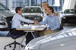 Foto: Car salesman and couple sitting at desk in large car showroom, two men shaking hands, smiling, side view Car salesman and couple sitting at desk in large car showroom, two men shaking hands, smiling, side view