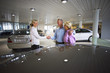 Photo: Car saleswoman and senior couple standing in large car showroom, saleswoman and man shaking hands, smiling, side view Car saleswoman and senior couple standing in large car showroom, saleswoman and man shaking hands, smiling, side view