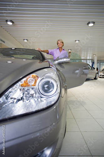 Photo: Senior woman looking at new silver convertible car in large showroom, front view, portrait Senior woman looking at new silver convertible car in large showroom, front view, portrait
