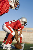 Photo: American football running back crouching with ball in scrimmage line during competitive game, side view (surface level) American football running back crouching with ball in scrimmage line during competitive game, side view (surface level)