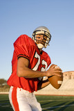Photo: American football quarterback, in red strip, looking to throw ball during competitive game, front view American football quarterback, in red strip, looking to throw ball during competitive game, front view