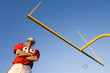 Photo: American football player, in red football strip and protective helmet, standing below goal post, arms folded, portrait, low angle view American football player, in red football strip and protective helmet, standing below goal post, arms folded, portrait, low angle view