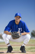 Photo: Baseball player wearing blue uniform, protective glove and cap, crouching on pitch, smiling, front view, portrait Baseball player wearing blue uniform, protective glove and cap, crouching on pitch, smiling, front view, portrait
