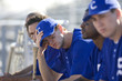 Photo: Dejected baseball team, in blue uniform, sitting on bench in stand during competitive baseball game, side view (differential focus) Dejected baseball team, in blue uniform, sitting on bench in stand during competitive baseball game, side view (differential focus)