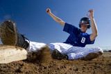Photo: Baseball player, in blue uniform, sliding safely into base on pitch during competitive game (surface level, blurred motion) Baseball player, in blue uniform, sliding safely into base on pitch during competitive game (surface level, blurred motion)