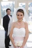 Foto: Bride and groom posing at wedding, focus on bride in wedding dress in foreground, smiling, front view, portrait Bride and groom posing at wedding, focus on bride in wedding dress in foreground, smiling, front view, portrait