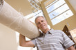 Senior man carrying rolled-up carpet on shoulder, moving house, smiling, low angle view, portrait