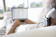 Photo: Senior man relaxing on sofa at home, listening to music on headphones, using laptop, rear view, focus on foreground Senior man relaxing on sofa at home, listening to music on headphones, using laptop, rear view, focus on foreground