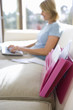 Photo: Mature woman sitting on sofa at home, using laptop, side view, focus on pink folder in foreground Mature woman sitting on sofa at home, using laptop, side view, focus on pink folder in foreground